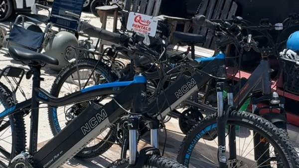 Black and blue electric bikes parked in front of a Quicky Cycles rental sign.