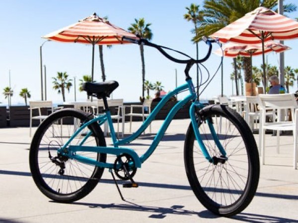 Blue bike parked on a sunny patio with palm trees and umbrellas.
