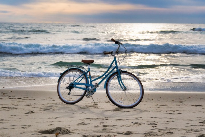 A blue bicycle on a sandy beach with ocean waves and a cloudy sky in the background.
